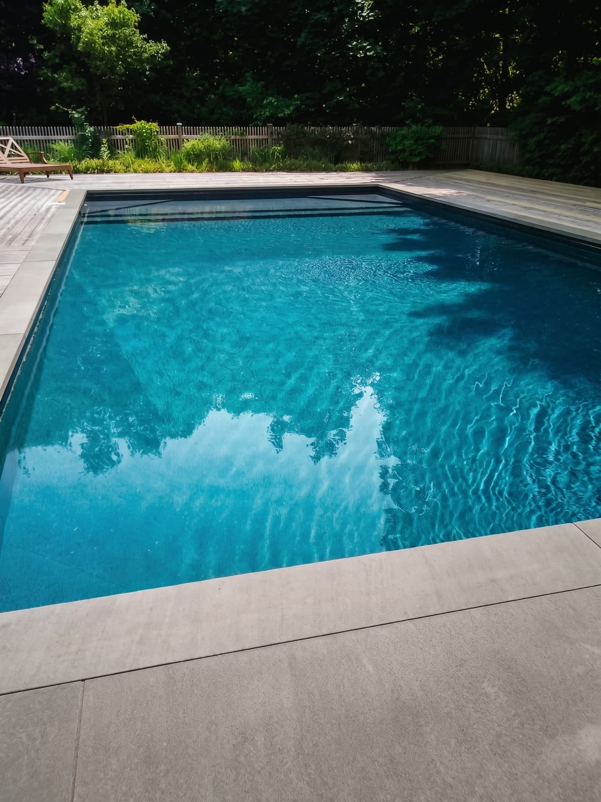 Inground pool framed by a natural wood deck and lush landscaping